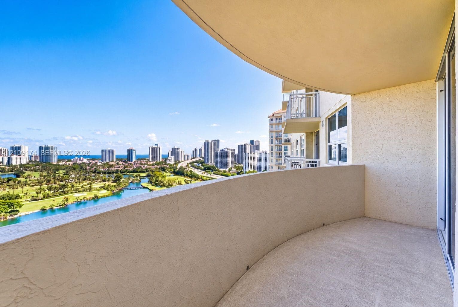 Covered balcony featuring a curved concrete wall, textured stucco finish, and panoramic scenery including a waterway, golf course, and cityscape
