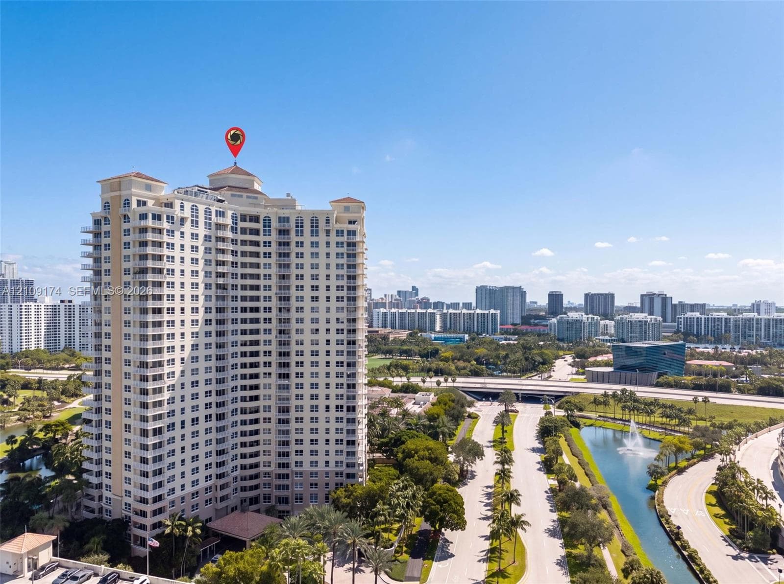 High-rise residential tower featuring multiple private balconies, a peaked roofline, and landscaped grounds with a water feature