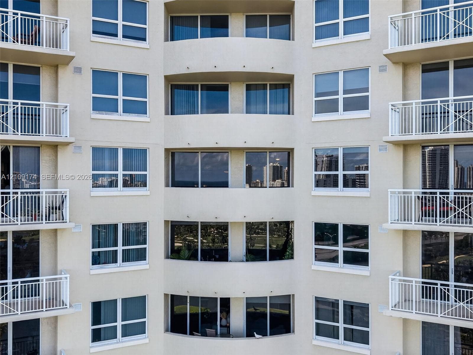 Multi-story high-rise exterior featuring a symmetrical facade, stucco finish, large glass windows, and private balconies with white railings