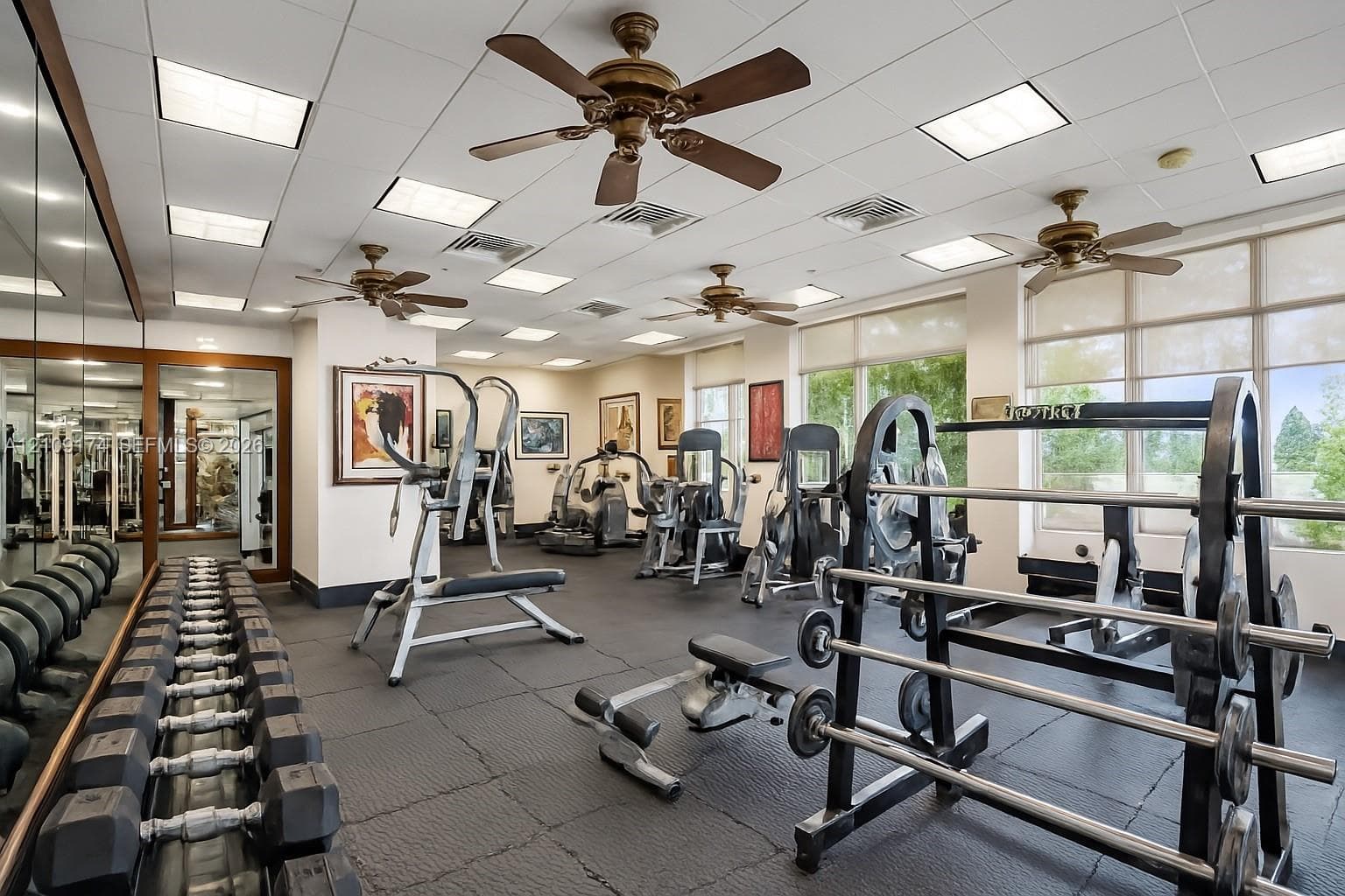 Fitness room featuring industrial rubber flooring, recessed panel lighting, mirrored wall, and multiple ceiling fans