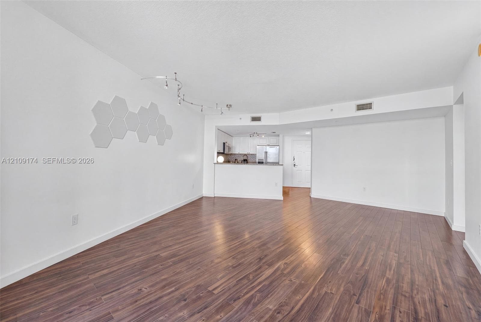 Open-concept interior featuring wood-finish flooring, white walls, integrated track lighting, and a breakfast bar counter