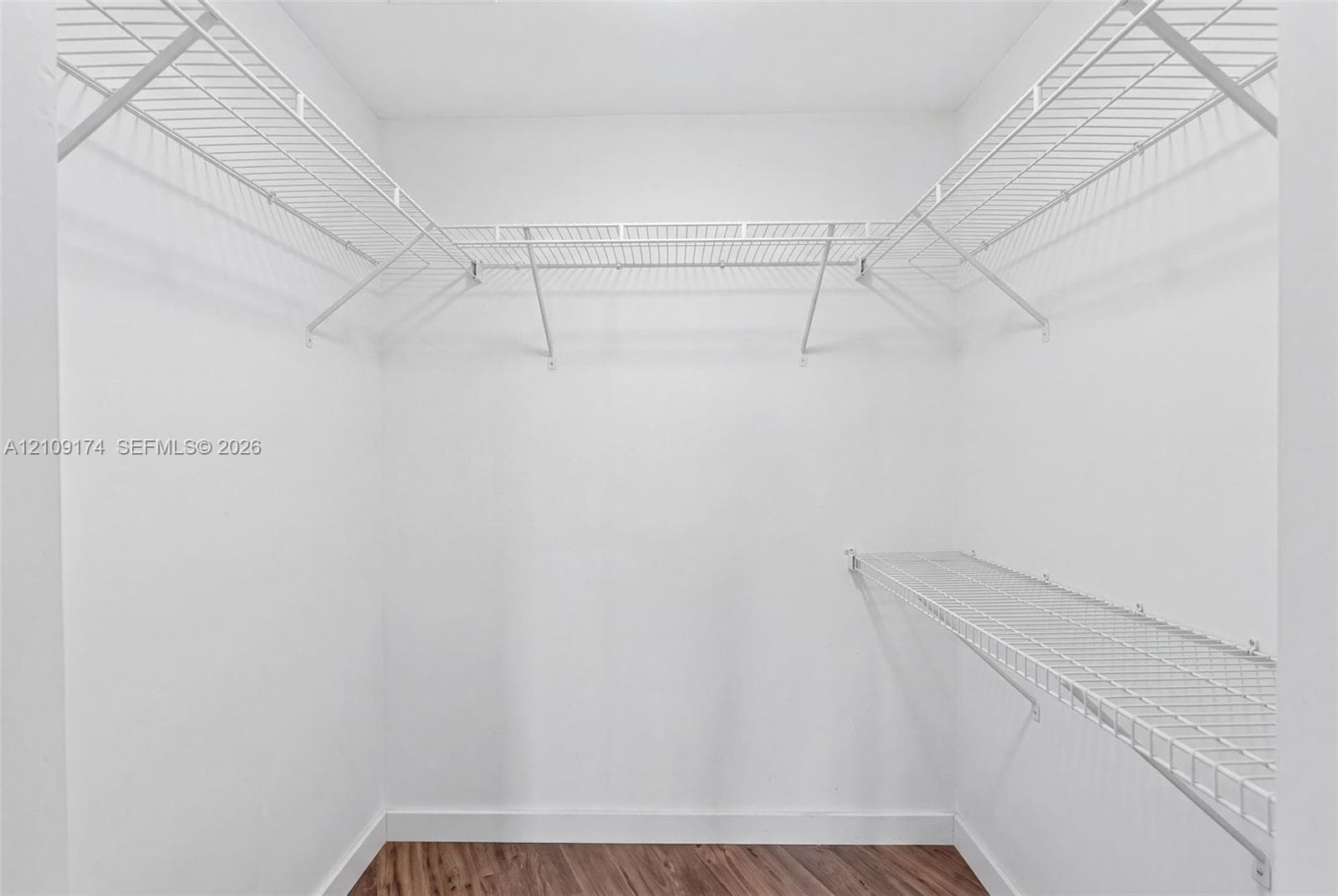 Walk-in storage space featuring wood-finish flooring and tiered white wire shelving