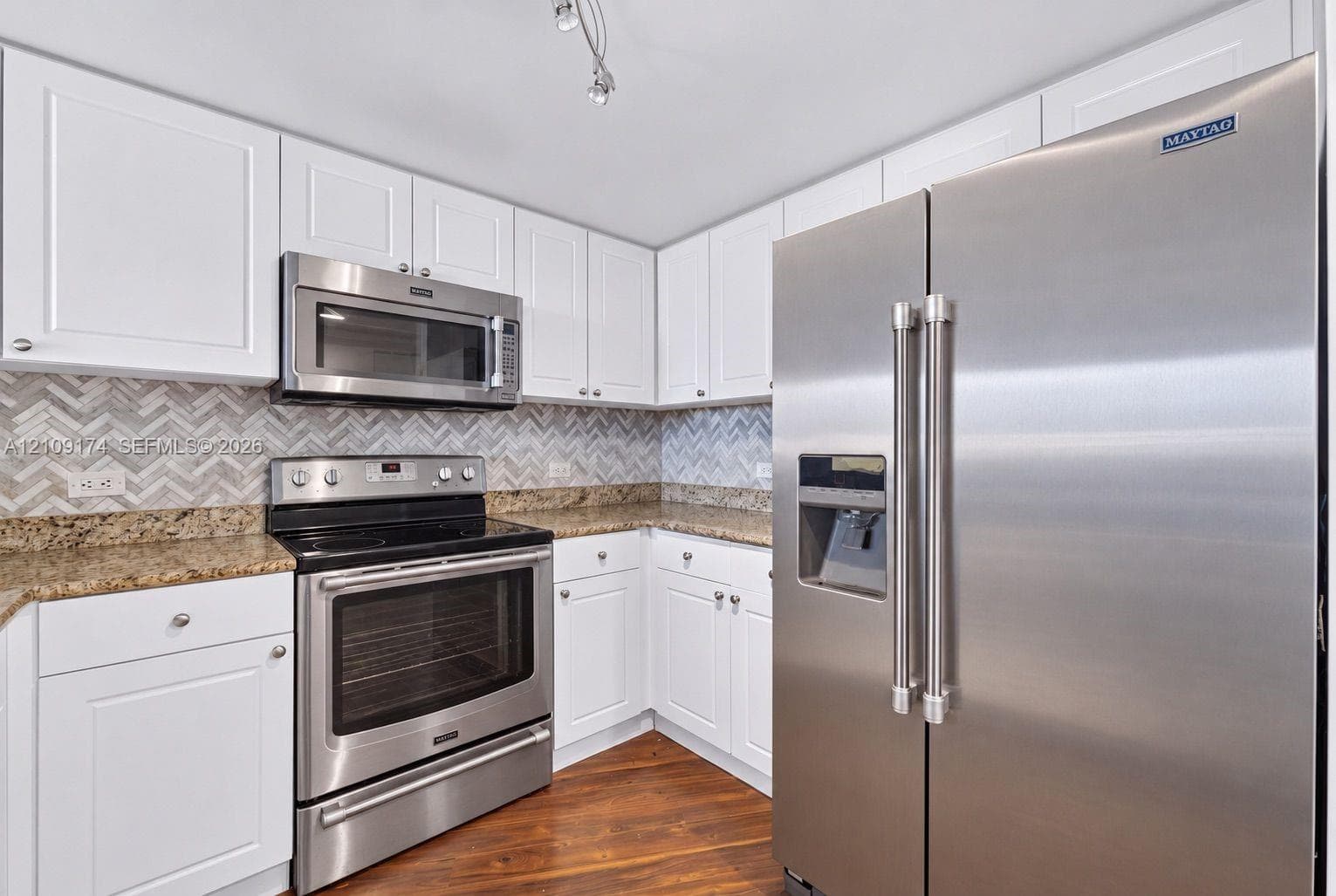 Kitchen featuring stainless steel appliances, white cabinetry, stone-finish countertops, and a herringbone-patterned tile backsplash