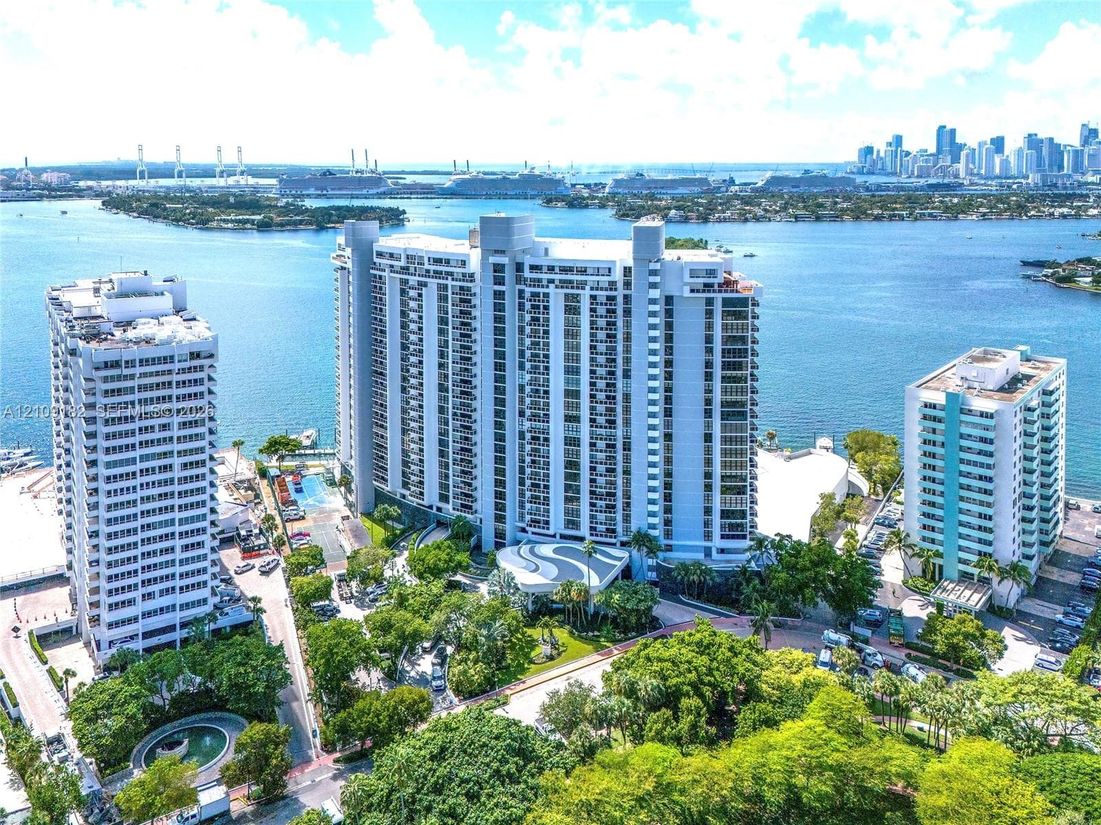 High-rise residential building featuring expansive water frontage, deep-water bay access, mature tropical landscaping, and integrated parking facilities