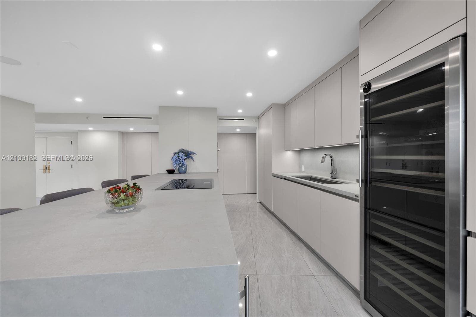 Contemporary kitchen featuring flat-panel cabinetry, a stone-finish waterfall edge island, a built-in wine refrigerator, integrated cooktop, and neutral large-format tile flooring