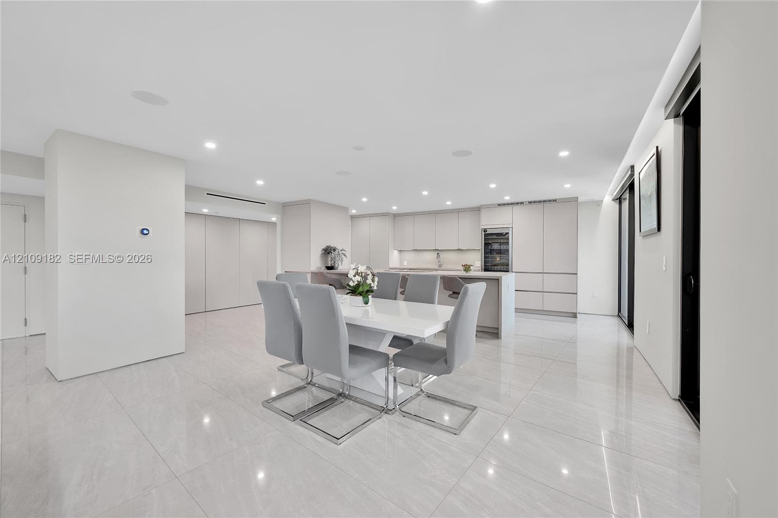 Open-concept kitchen and dining area featuring large-format tile flooring, flat-panel cabinetry, a central island with integrated seating, recessed lighting, and a built-in wine refrigerator