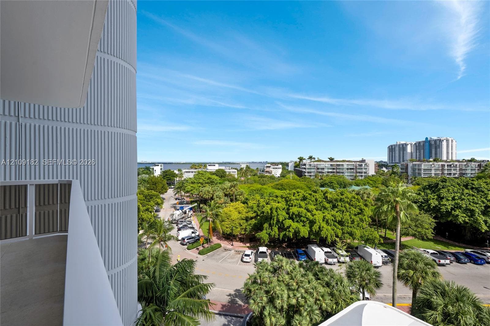 Private balcony featuring vertical ribbed architectural paneling and a metal railing, overlooking urban surroundings and mature trees