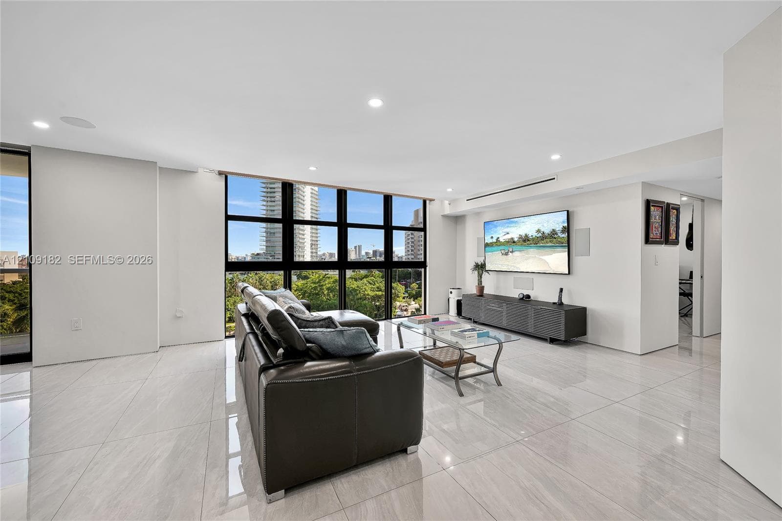Living area featuring large-format light-toned tile flooring, recessed ceiling lighting, and floor-to-ceiling windows with black framing