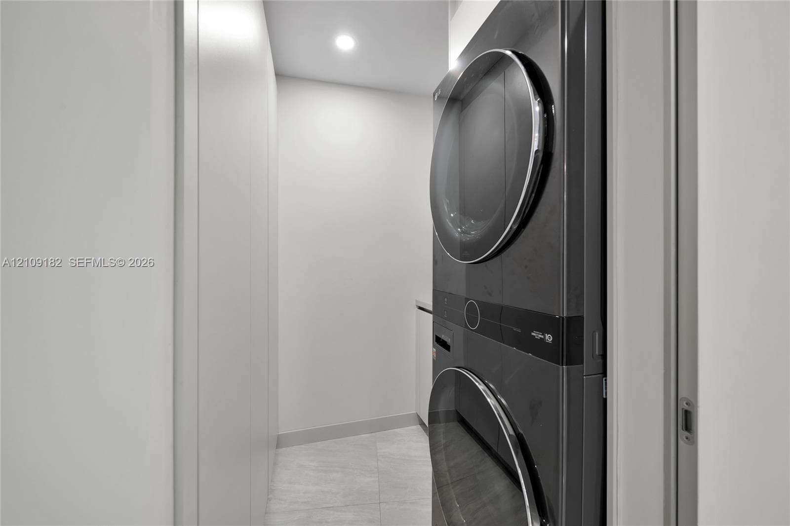 Stacked charcoal-toned laundry unit with recessed lighting, integrated cabinetry, and stone-finish tile flooring