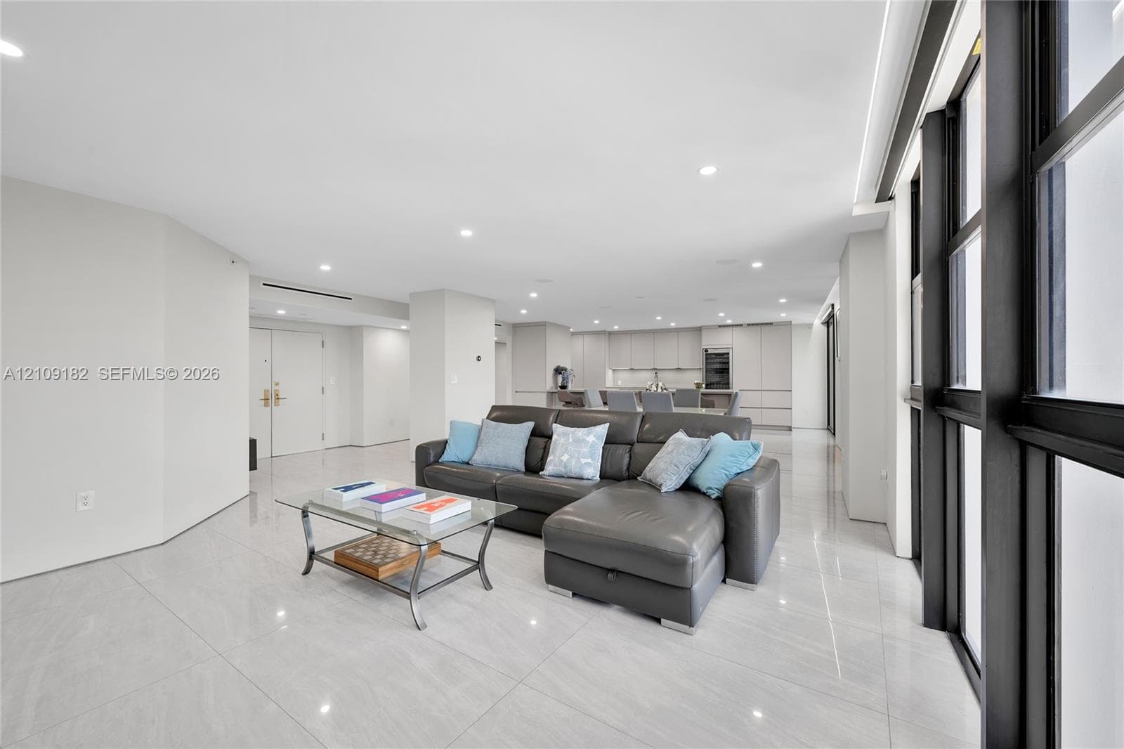 Open-concept interior featuring large-format tile flooring, recessed lighting, floor-to-ceiling windows with black metal frames, and flat-panel cabinetry