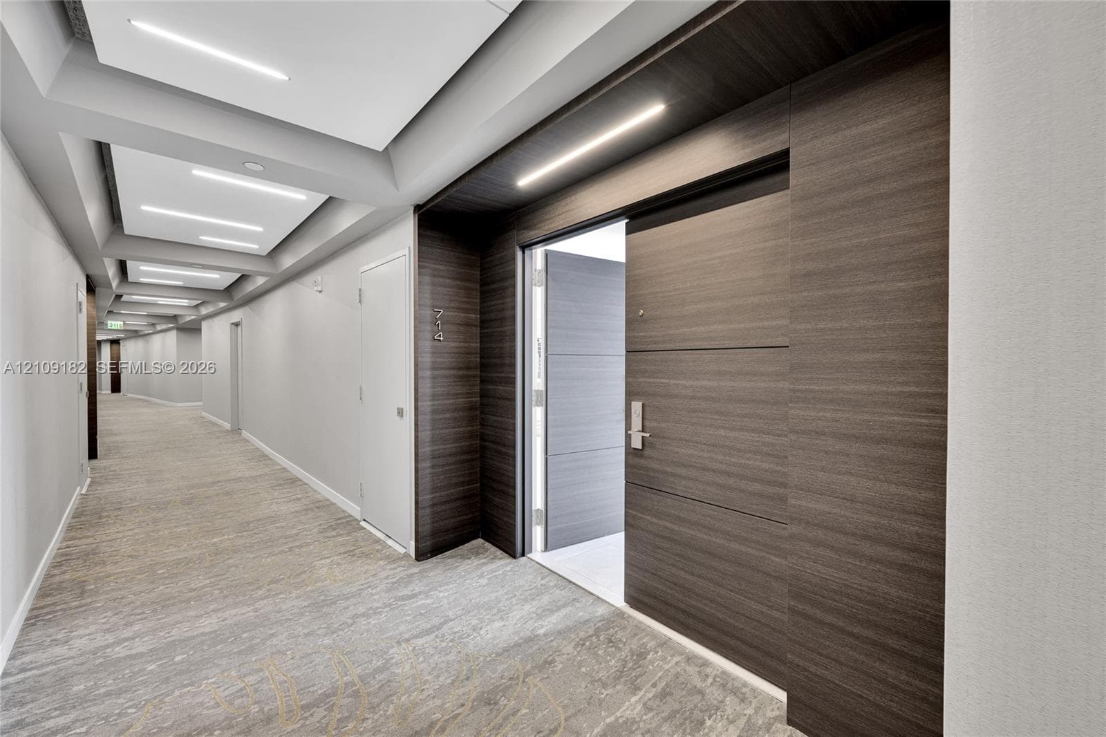 Hallway featuring wood-finish paneling, inset LED ceiling lighting, recessed tray ceiling details, patterned carpeting, and a wood-finish entry door with metal hardware