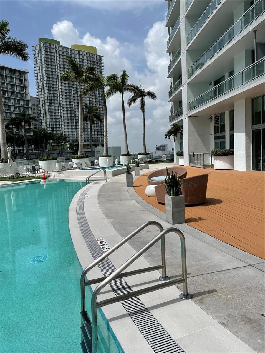 Curved swimming pool featuring a concrete deck and wood-finish terrace, stainless steel pool ladder, and integrated landscape planters