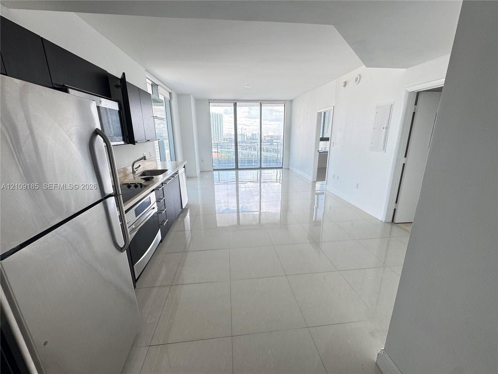 Kitchen area featuring dark cabinetry, stainless steel appliances, and tile flooring, highlighted by floor-to-ceiling windows