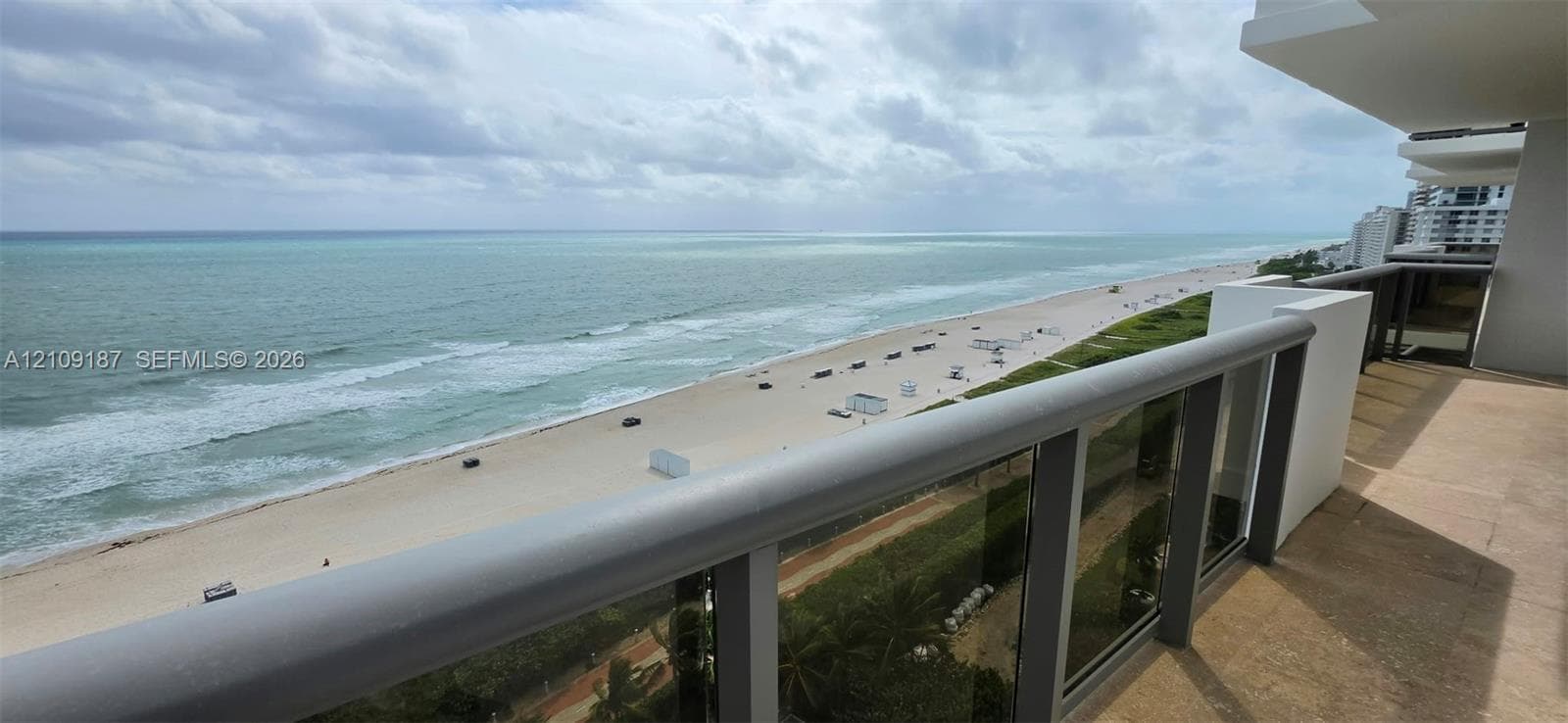 Private balcony with marble flooring and a glass-paneled railing overlooking the coastline and direct front 180° ocean view.