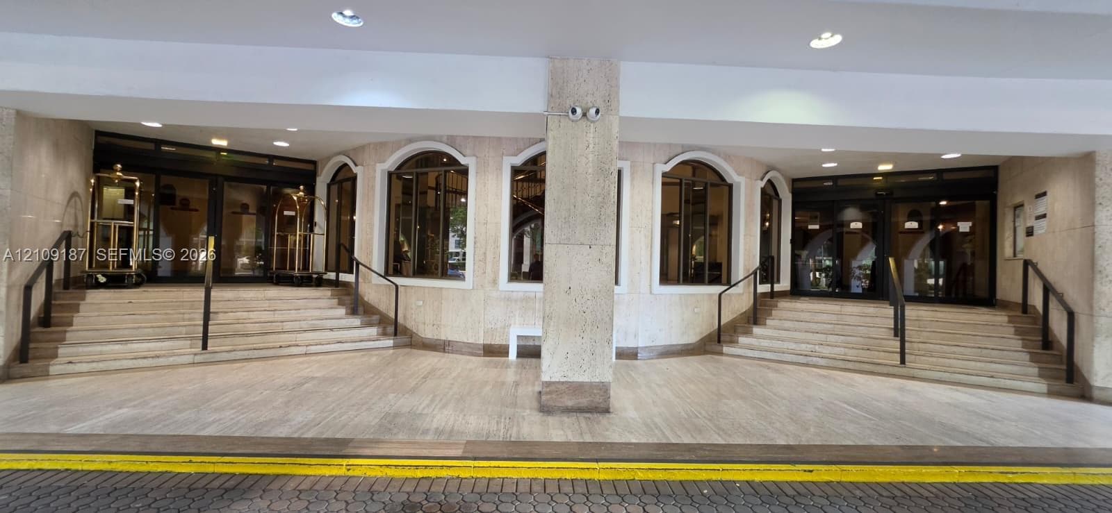 Building covered main entrance and valet parking, featuring marble facade, arched windows, dual staircases with metal handrails, and multi-pane glass entry doors