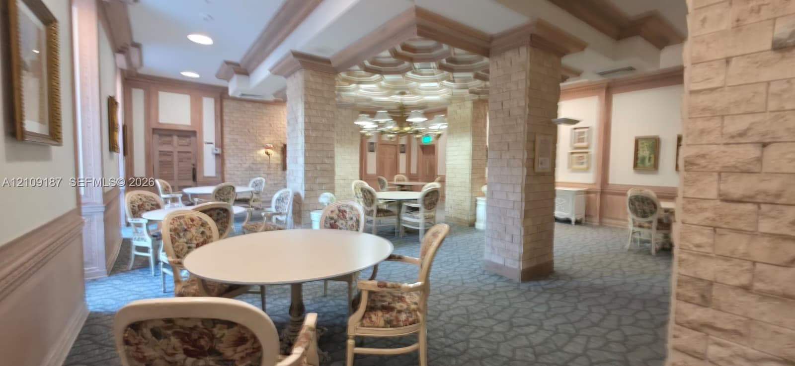 Women's playroom featuring ornate tiered tray ceilings, decorative masonry pillars, layered crown molding, and recessed lighting.