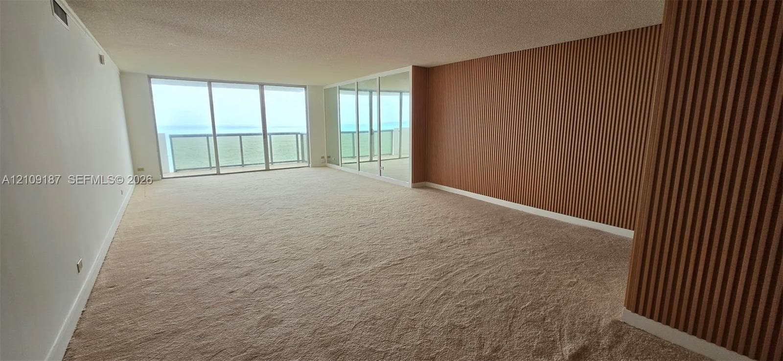 Open-concept space featuring floor-to-ceiling windows, mirrored wall panels to enhance panoramic ocean view, and wood-slat accent wall detailing