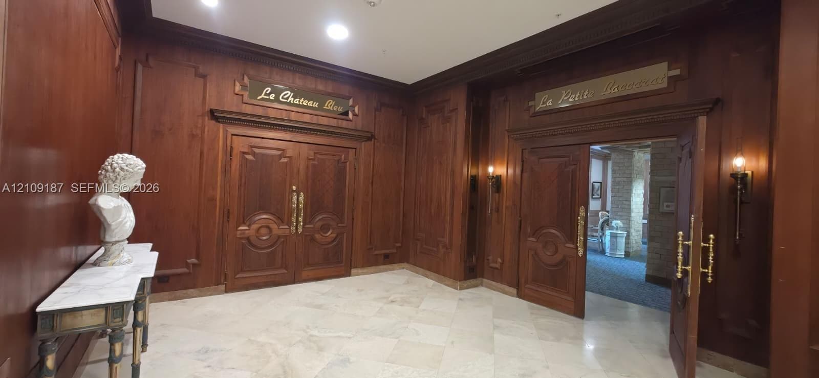 Elegant great room Featuring wood-paneled walls, intricate double wooden doors, marble flooring, and wall-mounted brass light fixtures.
