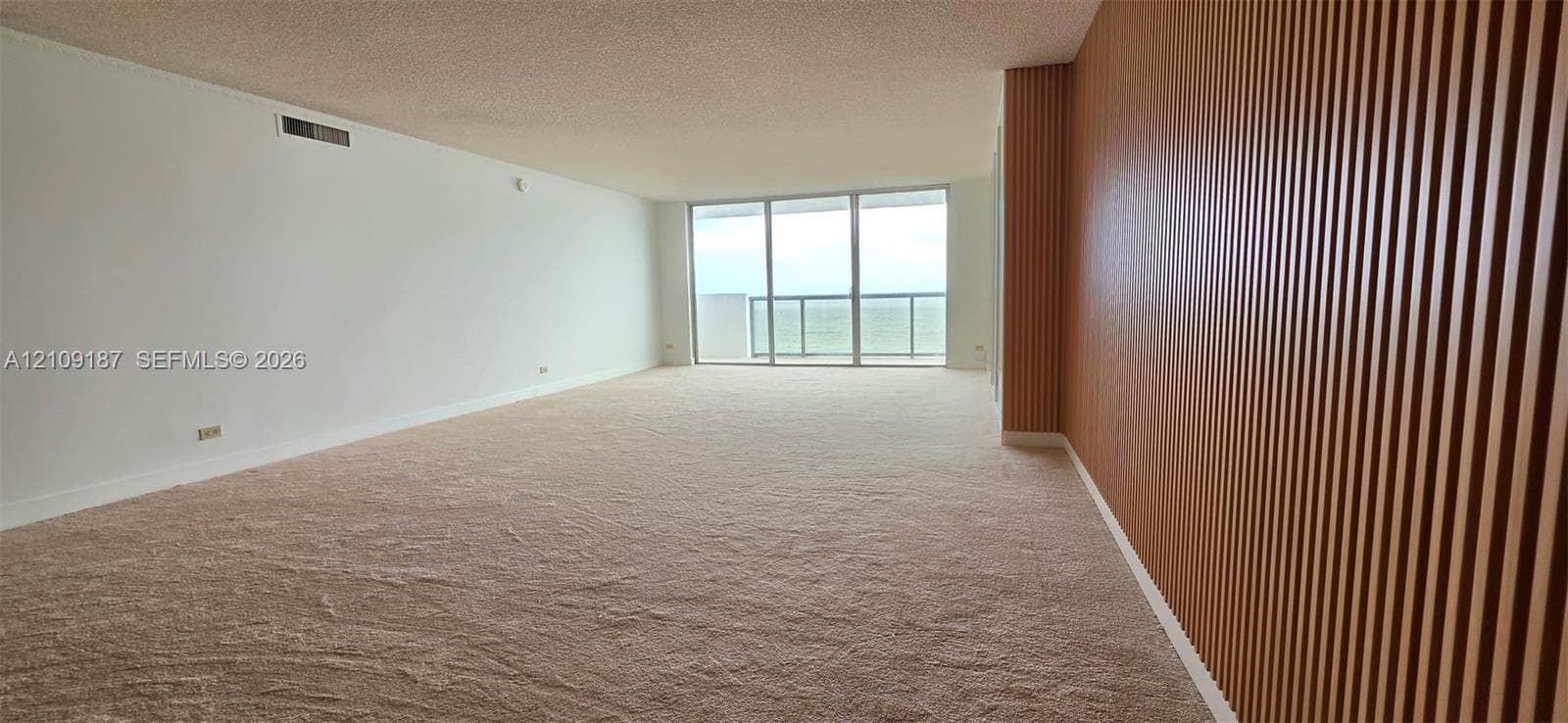 Floor-to-ceiling glass sliding doors to balcony and direct front ocean view, wall-to-wall carpeting, and a custom vertical wood-slat accent wall