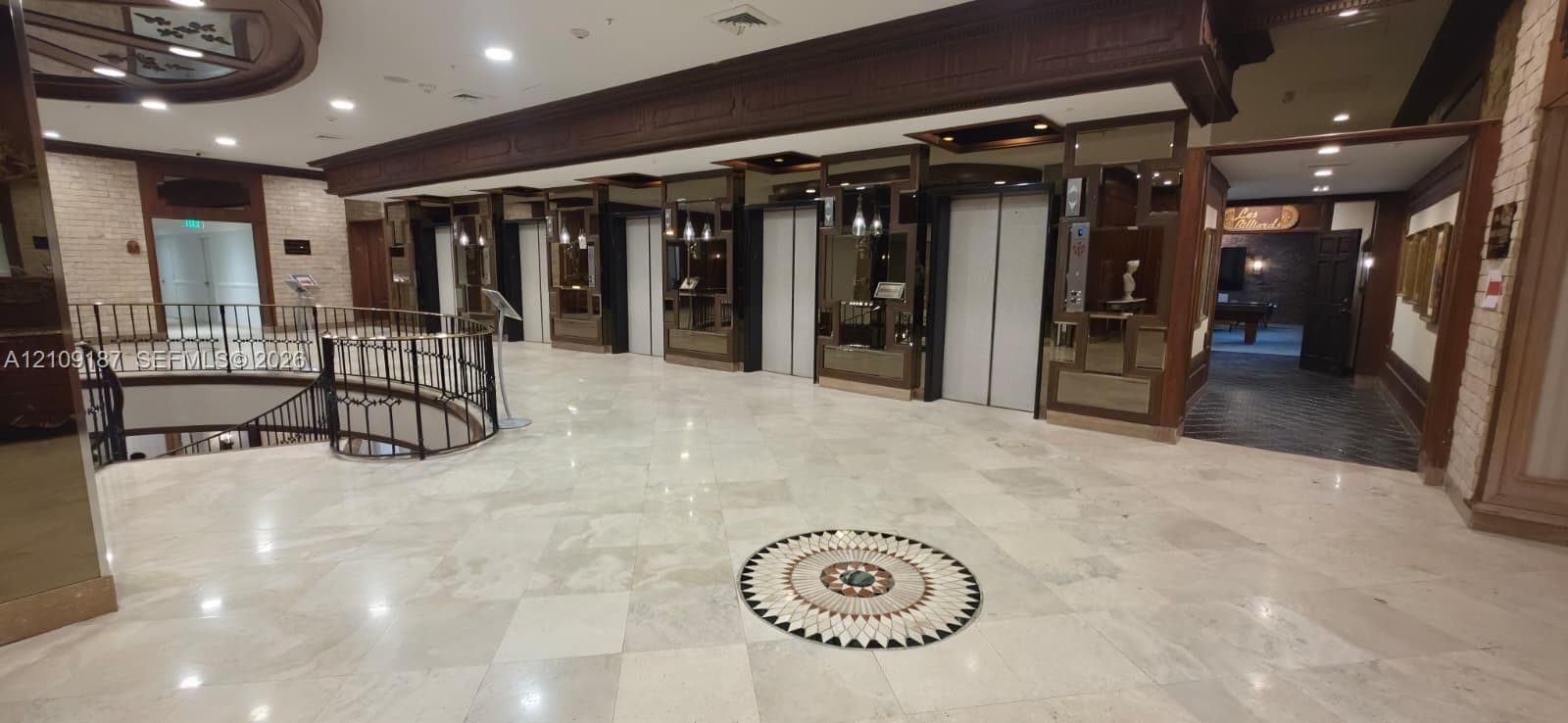 Grand lobby featuring marble flooring with decorative inlay, multi-elevator bank, ornate iron stair railing, and wood-paneled accents