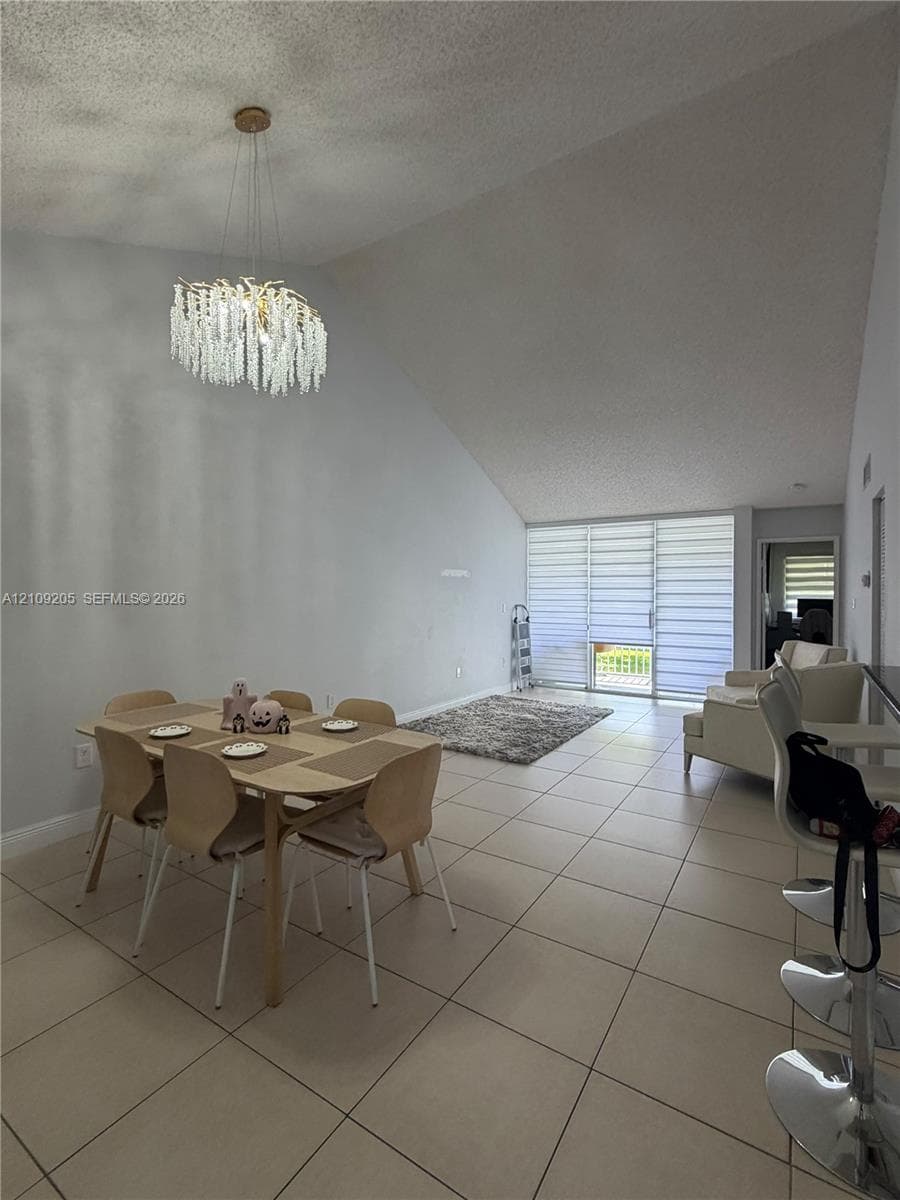 Vaulted ceilings, large-format tile flooring, decorative beaded chandelier, and floor-to-ceiling glass sliding doors with integrated shades