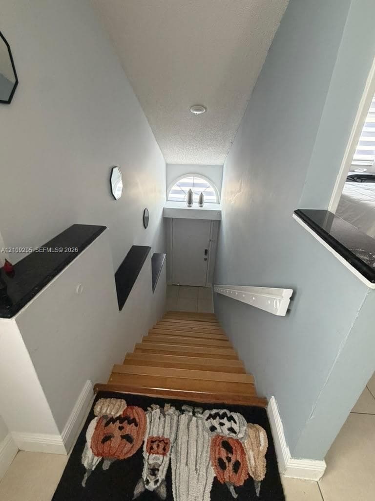 Staircase featuring wood-finish treads, stone-topped wall ledges, and a semi-circular transom window