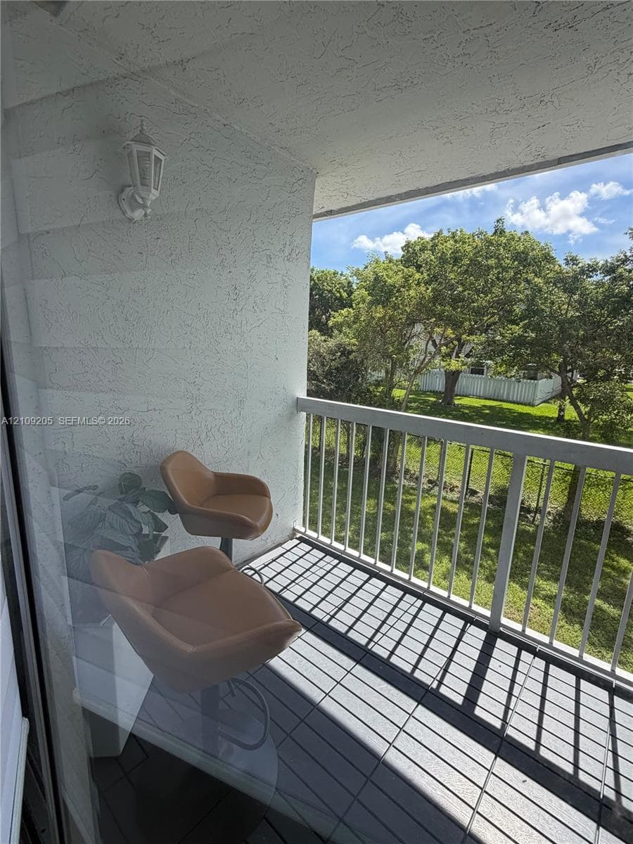 Private balcony featuring white vertical railing, textured stucco walls, overhead carriage-style lighting, and tiled flooring