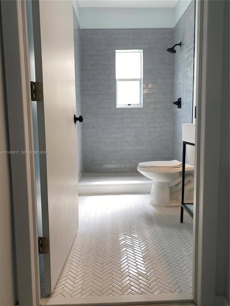 Bathroom featuring herringbone-patterned tile flooring, subway-tiled shower surround, and matte black plumbing fixtures