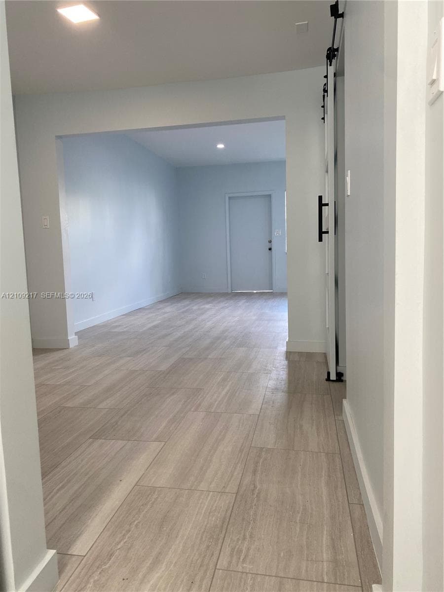 Wood-finish tile flooring, white sliding barn door with matte black hardware, and recessed lighting