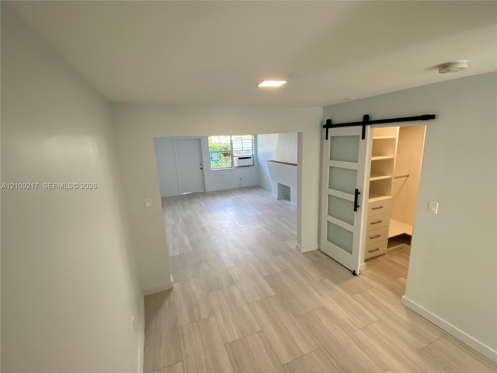 Light-toned tile flooring throughout, sliding barn door with frosted glass panels, and built-in closet cabinetry featuring shelving and drawers