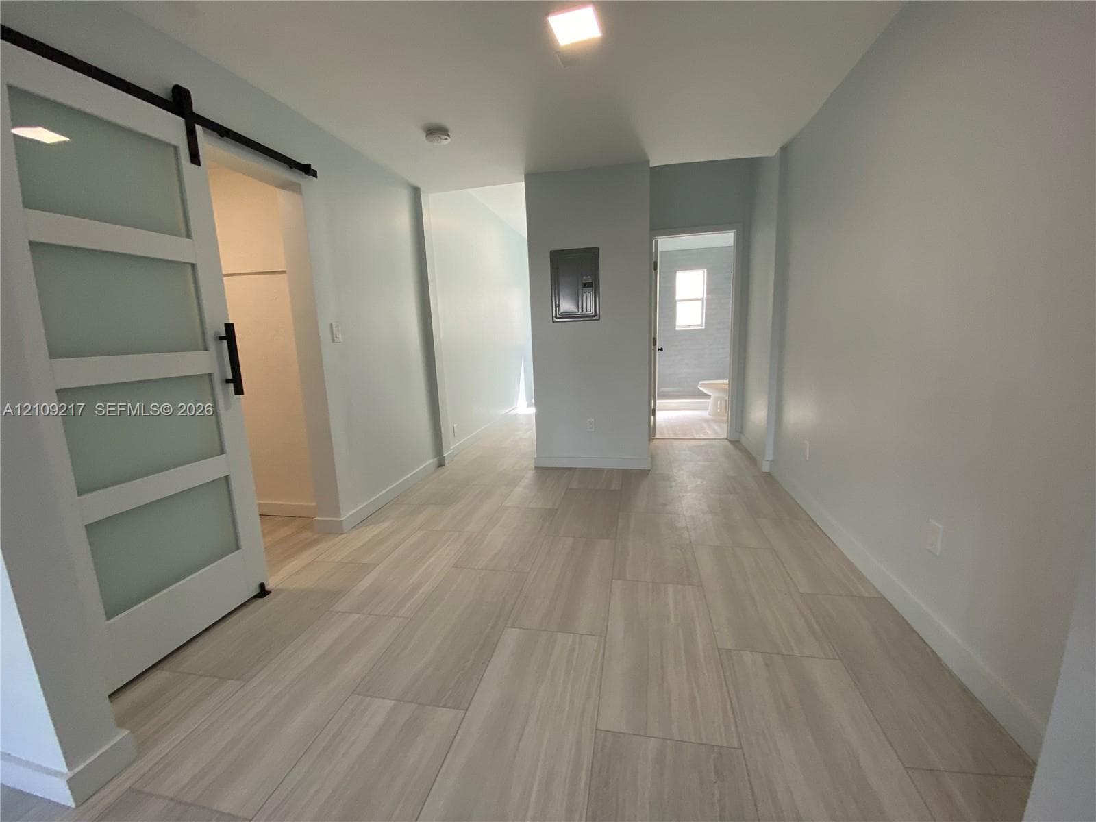 Sliding barn-style door with frosted glass panels, wood-finish tile flooring, recessed ceiling lighting, and neutral wall tones
