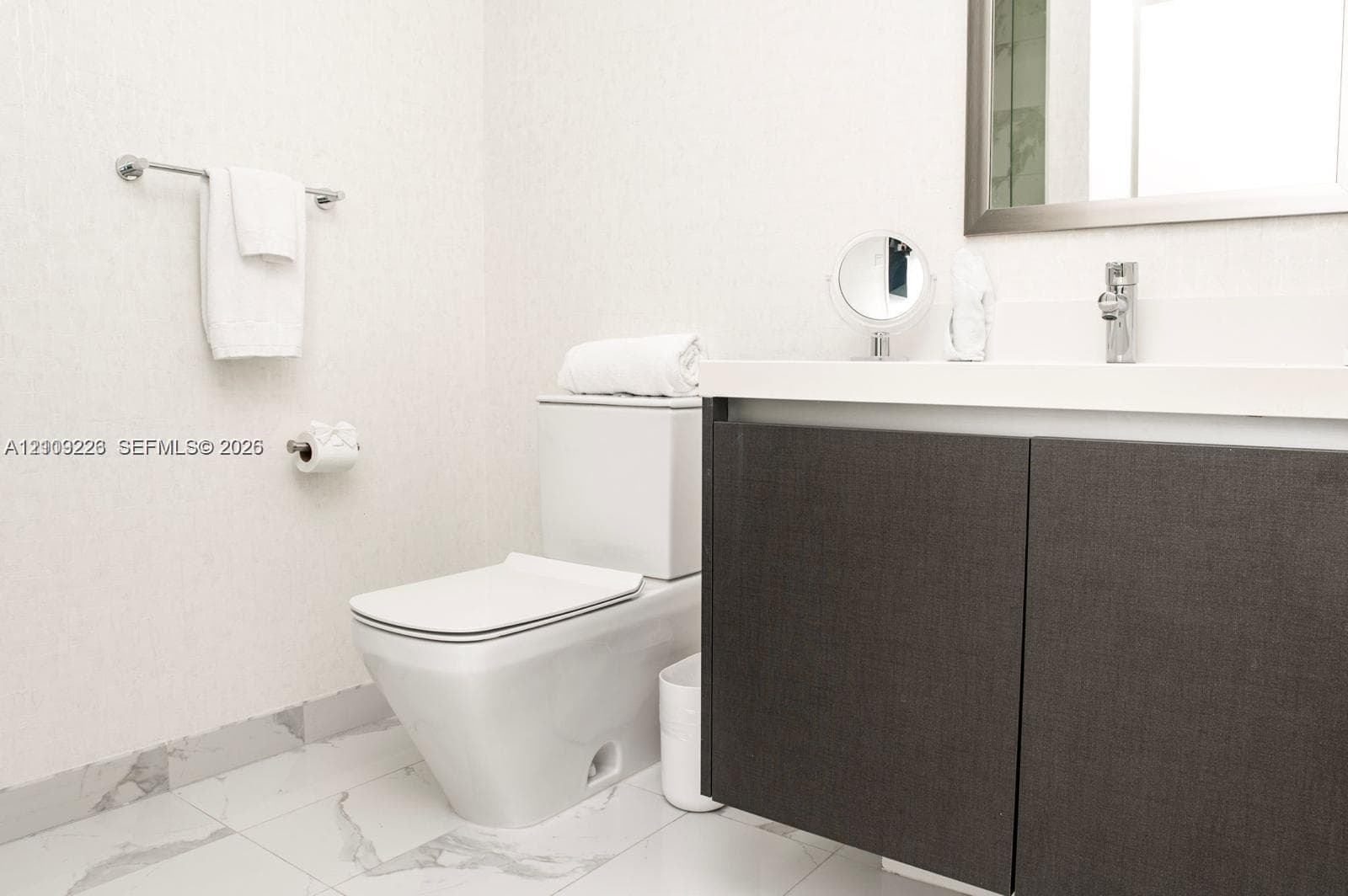 Modern floating vanity with a solid-surface countertop and integrated sink, complemented by a dual-tone charcoal cabinet, chrome-finished wall-mounted faucet, and polished stone-finish floor tiling