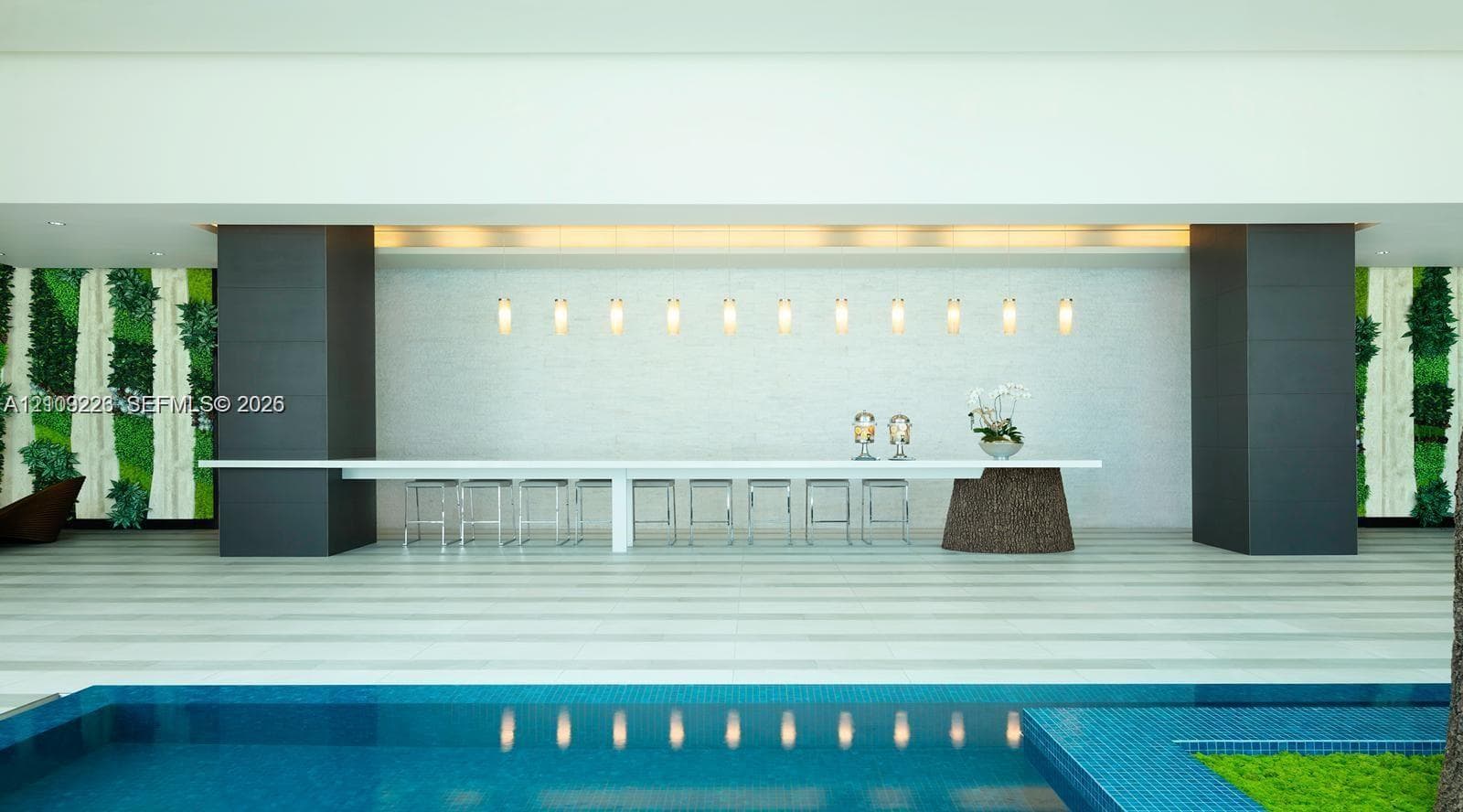 Custom long-format counter with a stone pedestal base, linear pendant lighting, textured feature wall, and integrated vertical greenery accents, overlooking a tiled swimming pool