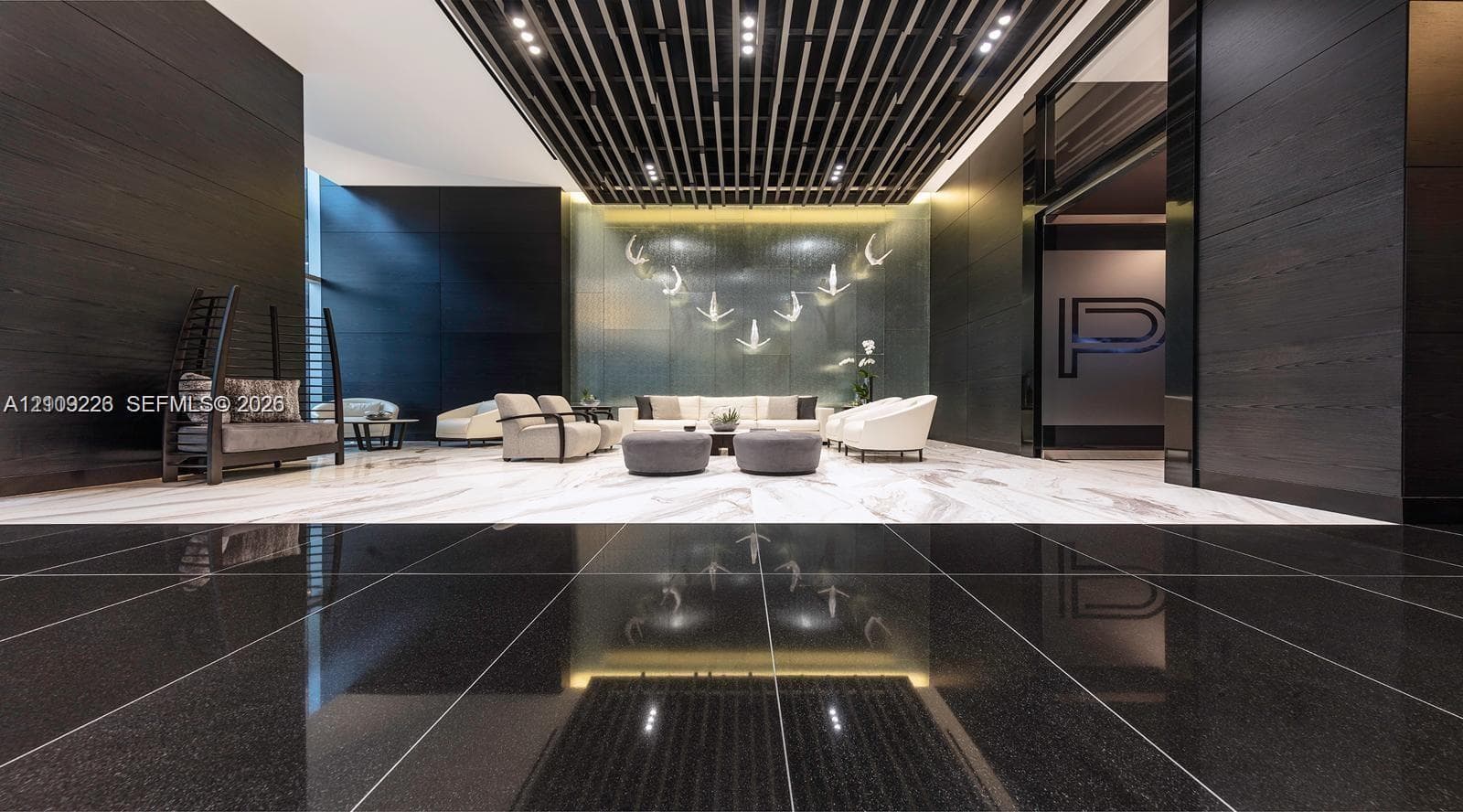 Grand lobby featuring polished stone flooring, dark wood-paneled walls, a suspended slatted ceiling, and an illuminated decorative feature wall
