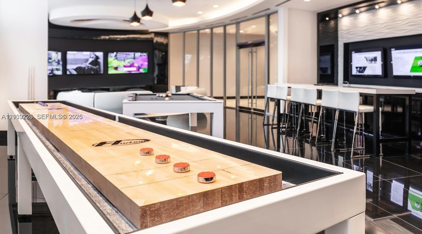 Recreational space featuring high-gloss flooring, recessed ceiling lighting, a built-in media wall with integrated displays, and floor-to-ceiling glass paneling