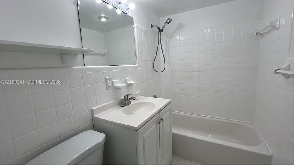 Bathroom featuring a white vanity cabinet with an integrated basin, a wall-mounted medicine cabinet with integrated lighting, and a full-height tiled shower surround