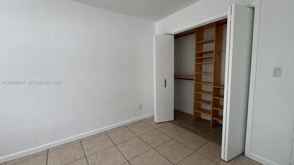 Room featuring neutral tile flooring, white walls, and a closet with custom built-in wooden shelving and a hanging rod