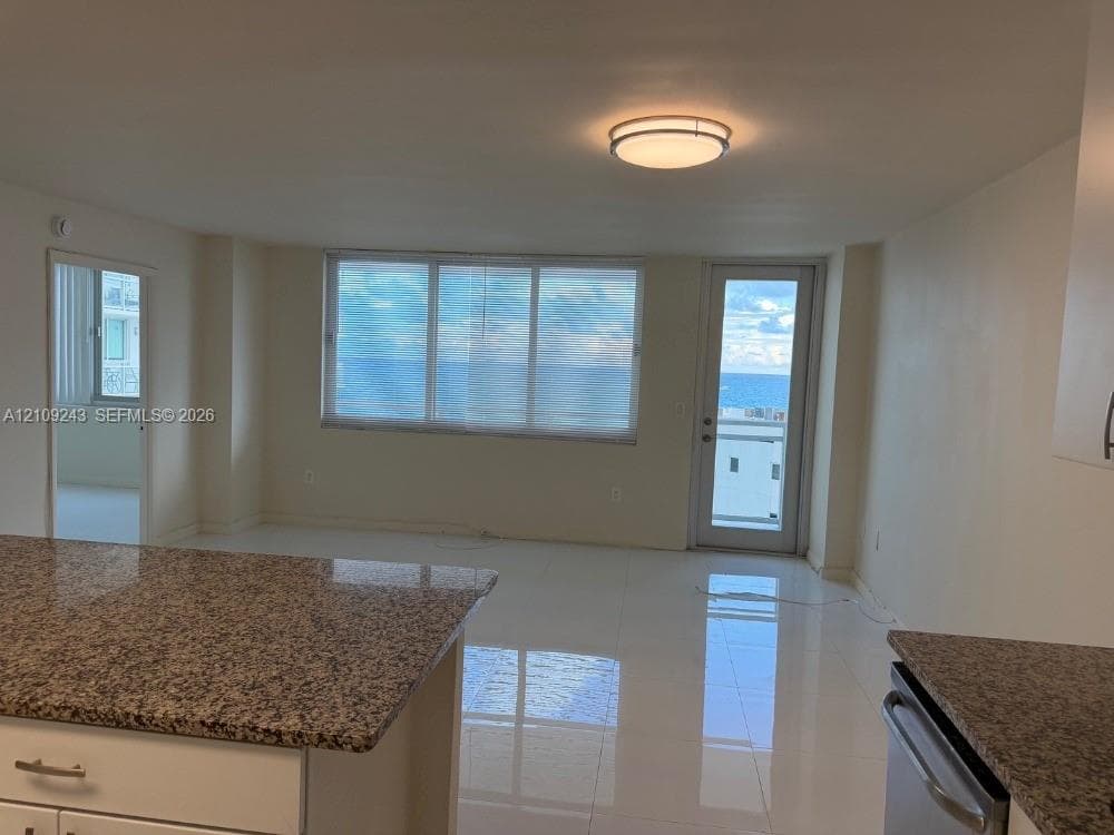 Open-concept area featuring stone-surface countertops, polished tile flooring, expansive windows, and a glass-paneled door