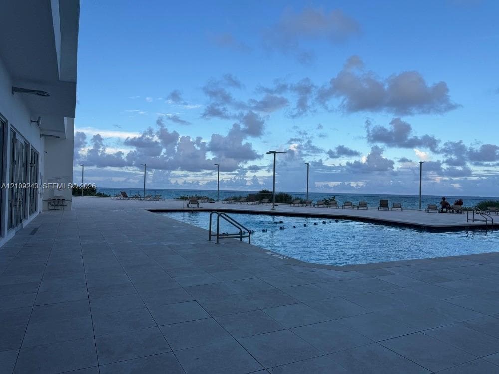 Swimming pool with a paved deck, metal railings, and integrated lighting fixtures, positioned against an ocean horizon