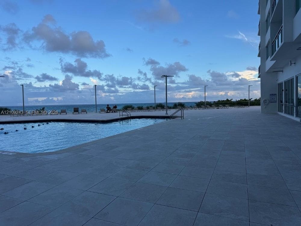 Outdoor swimming pool with tile surround and metal railings, set against an ocean backdrop