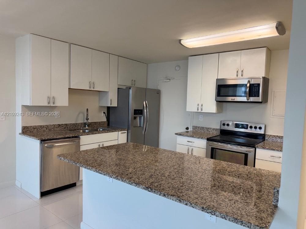 Kitchen featuring white cabinetry, stone countertops, stainless steel appliances, a central island, and tile flooring