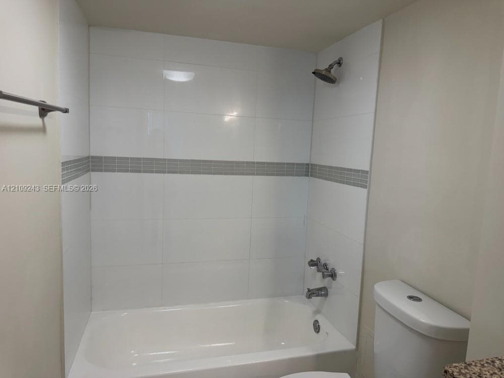 Bathtub shower combination featuring white rectangular wall tile, a decorative mosaic tile inlay, a chrome shower head, and a chrome faucet assembly