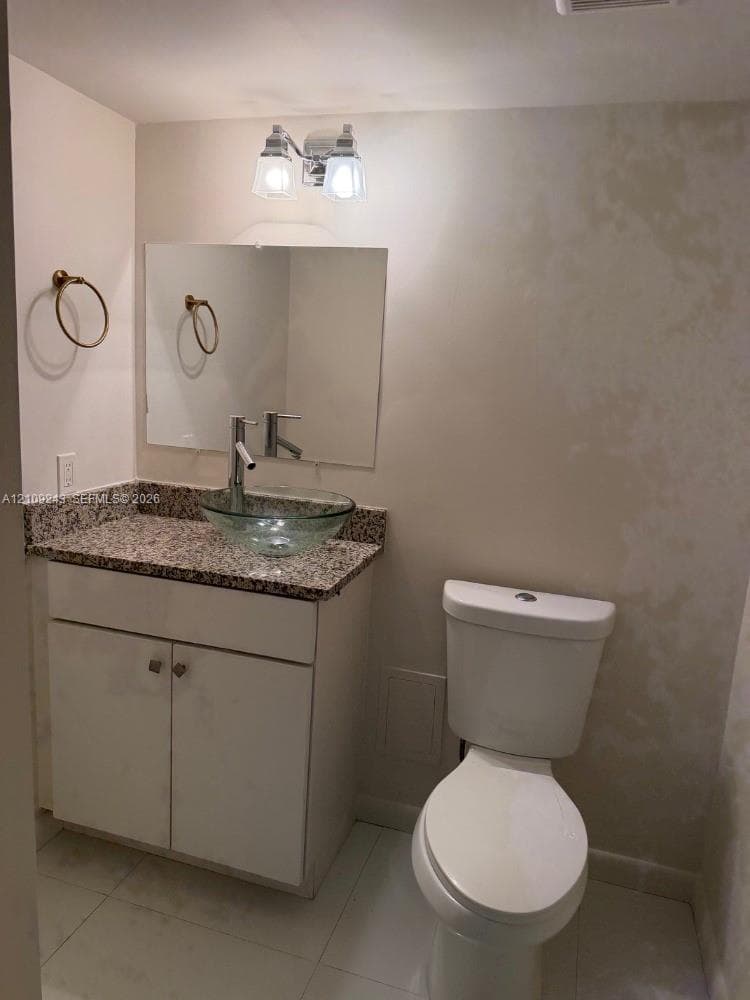 Half Bath. Vanity with stone countertop, clear glass vessel sink, tall metal faucet, wall-mounted mirror, and two-light fixture