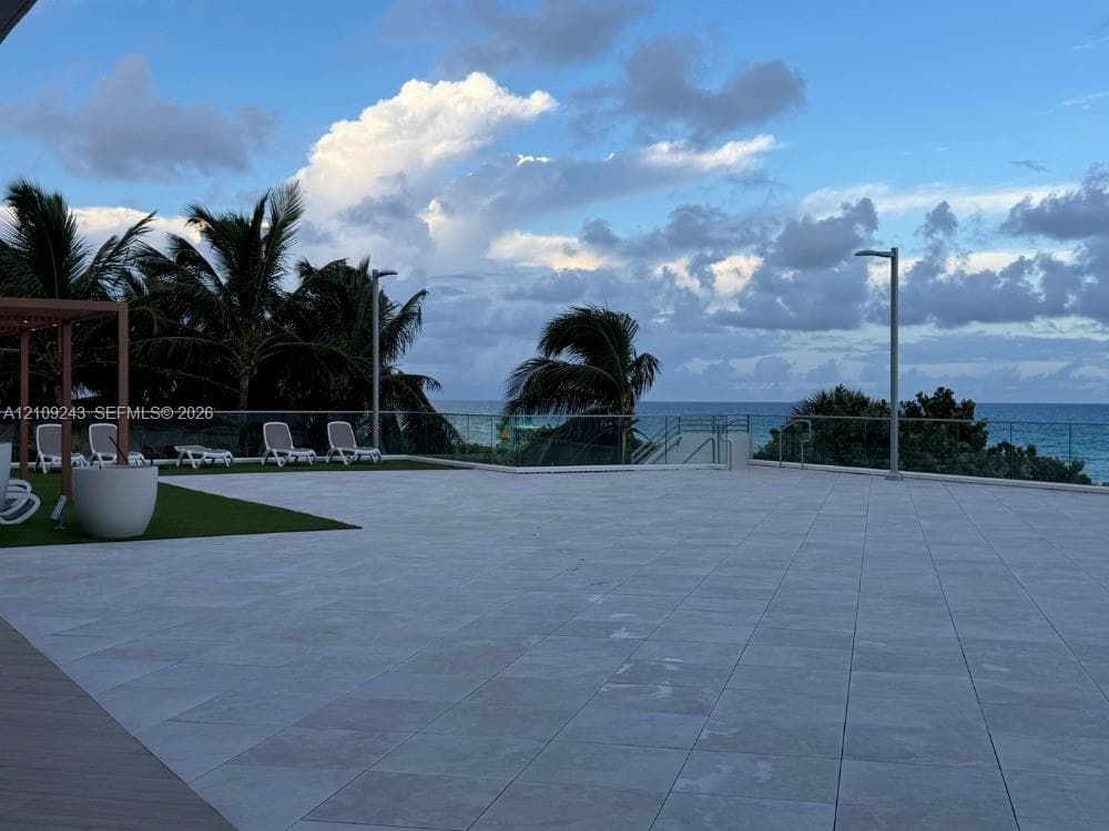 Expansive terrace featuring large-format tile flooring, integrated glass railing, and a pergola structure
