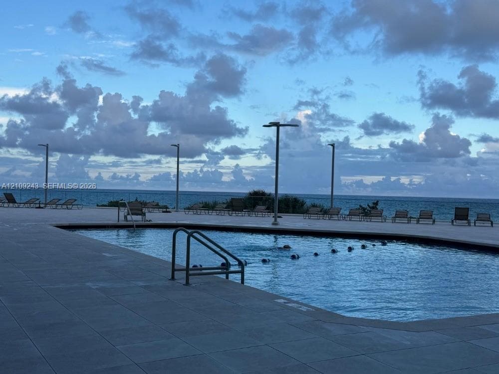 Swimming pool featuring tile decking and a metallic handrail, set against an ocean backdrop