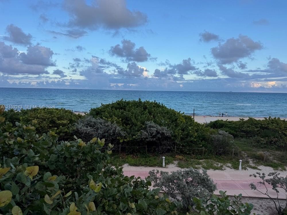 View from pool deck. Direct oceanfront exposure featuring native coastal vegetation, sandy shoreline, and a paved pedestrian pathway