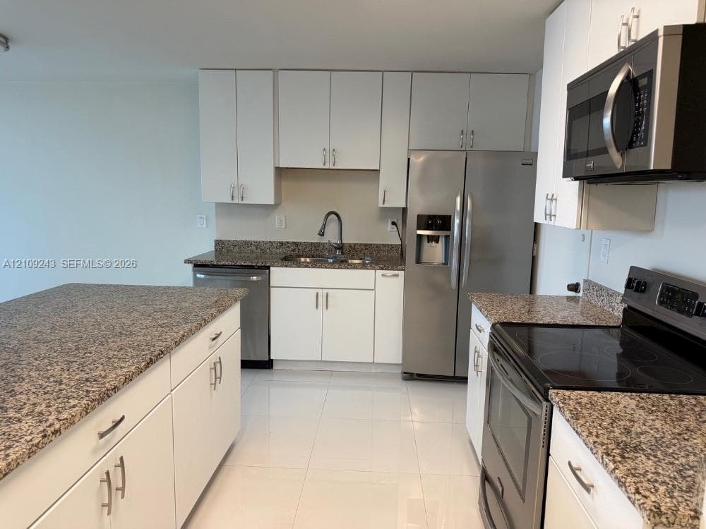 Kitchen featuring white cabinetry, stone countertops, stainless steel appliances, a central island, and tile flooring