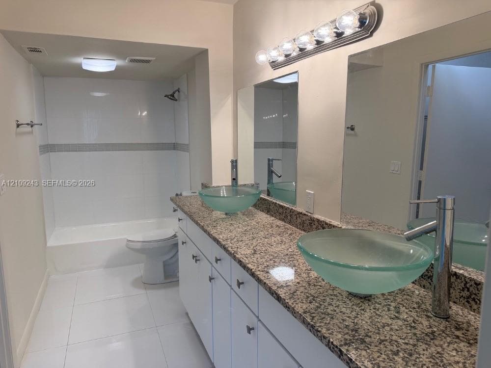 Dual vanity featuring frosted glass vessel sinks, stone-finish countertops, white cabinetry, and wall-to-wall mirrors