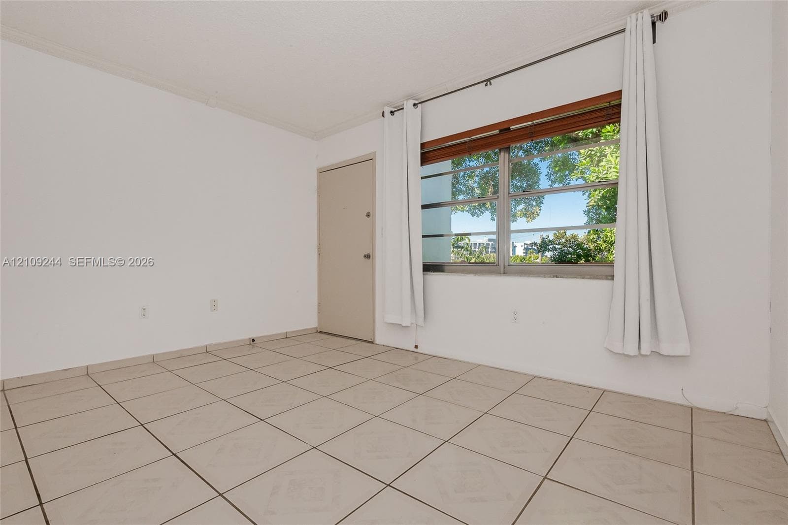 Neutral-toned ceramic tile flooring, solid-core interior door, and horizontal window with wood-finish blinds