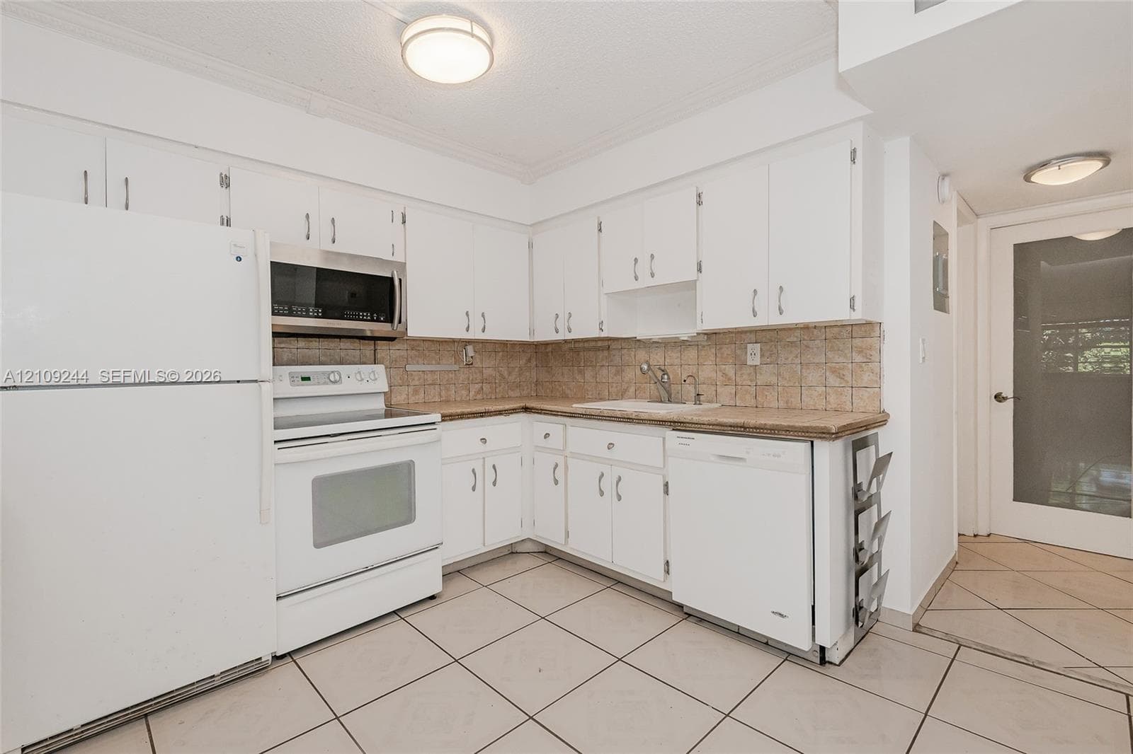 Kitchen featuring white cabinetry, solid-surface countertops, tile backsplash, tile flooring, and integrated white appliances